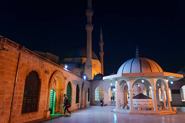 People walking in Mevlid Halil Mosque courtyard with illuminated historical architecture at night