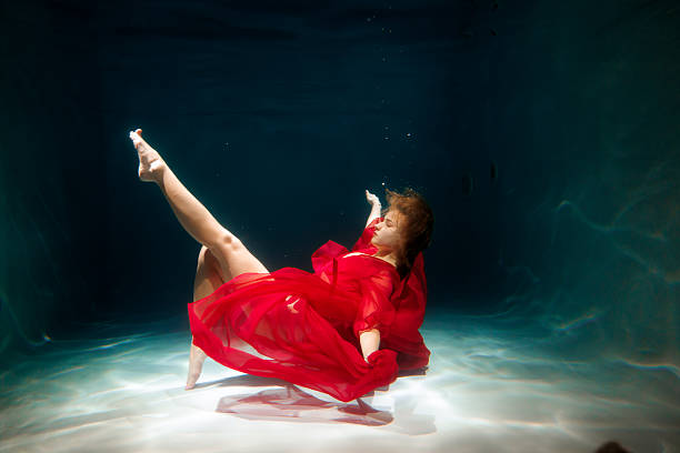 istock Lady in red beneath water, Redclad woman strikes pose underwater 2247833926