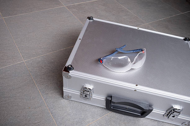 Protective goggles resting on a silver metal case on a tiled floor, highlighting safety equipment and modern industrial tools, horizontal