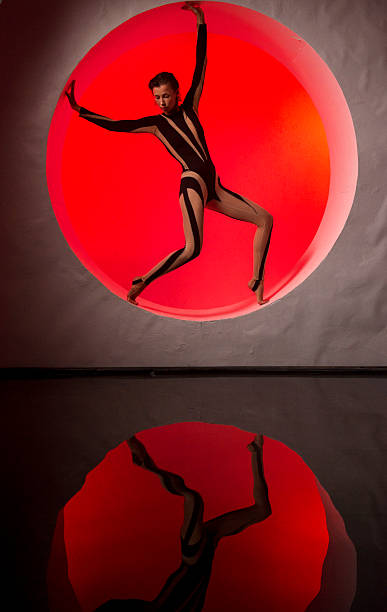 A slender, athletic woman poses in a studio against a red backdrop.