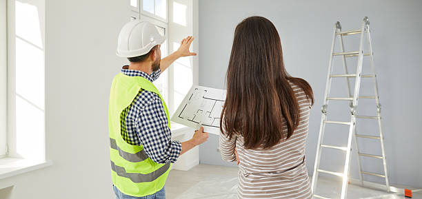 istock Architect or builder with blueprint plan pointing to wall and talking to woman about house design 2247843802