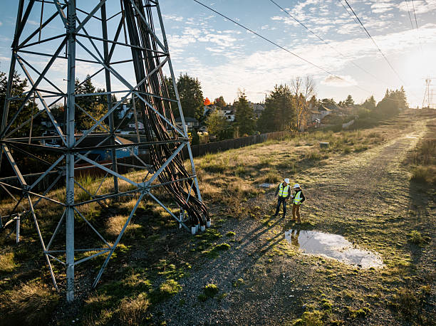 A Caucausan man working as a lineman examining the power grid, utilizing modern technology with a touchscreen tablet.  Hard working maintenance engineer career.  Shot in Washington state.  Drone point of view