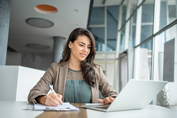 istock Young businesswoman multitasking at desk using laptop and writing notes 2247848441