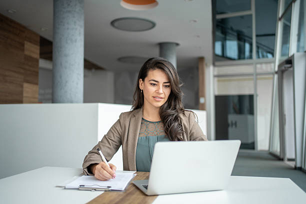 istock Young businesswoman working on laptop, writing notes in modern office 2247848443