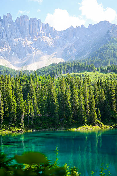 Turquoise water of lake carezza showing reflections of surrounding mountains and lush pine trees