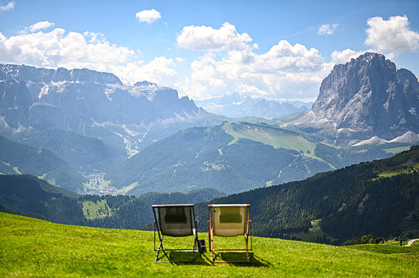 Two empty deck chairs overlooking a vast mountain range under a beautiful blue sky