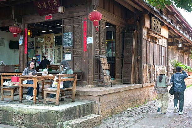 Shaxi, China - October 11th, 2025: Street scene of Shaxi ancient town in Jianchuan county, Yunnan province. View of people sitting in a corner restaurant and other tourists on the street.