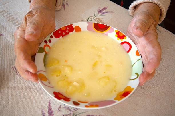 Traditional Hungarian potato stew in a bowl held by an elderly woman’s hand, close-up.