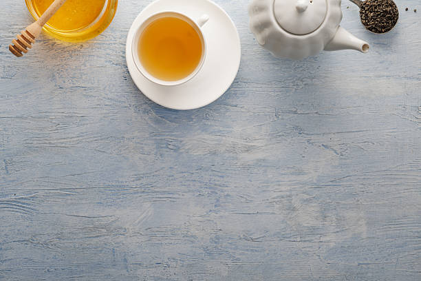 Fresh tea in a white ceramic cup, honey, honey spoon, teapot, tea leaves on the table.. Top view.