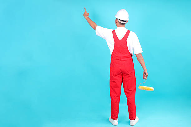 istock Back View of Painter Holding Roller Brush and Pointing to Empty Space Isolated on Blue Background 2247881346