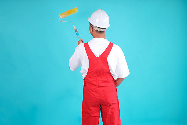 istock Back View of Skilled Construction Worker in Red Overalls Painting with Roller Brush 2247881399