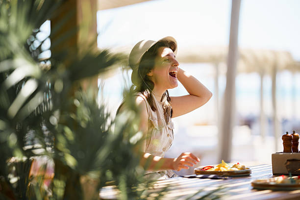 Woman laughing heartily enjoying food and summer lifestyle at an outdoor restaurant.