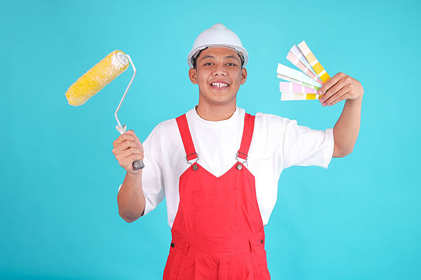istock Smiling Painter Man in Red Overalls Holds Paint Roller and Color Swatches, Ready for Project 2247881919