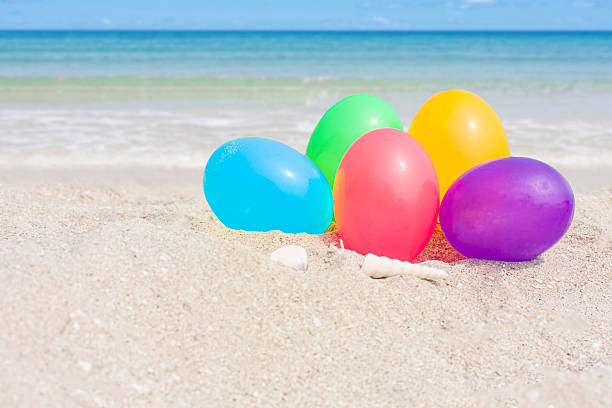 Colorful eggs on white sand beach over blue sea, happy Easter or summer holiday concept.
