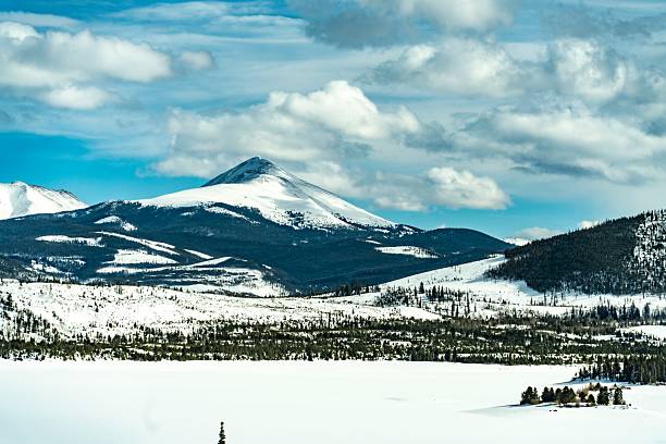 This stunning winter landscape showcases a vast snow-covered mountain range beneath a dynamic sky filled with clouds. The expansive snowfield in the foreground adds a sense of tranquility and openness, making it ideal for nature-themed projects, outdoor adventure promotions, and seasonal travel marketing. The crisp, cold atmosphere evokes a serene and peaceful mood perfect for winter tourism and environmental campaigns.