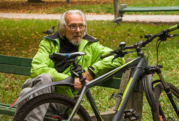 Man in the green jacket taking a break from cycling. Senior man is resting in the city park.Concept of healthy lifestyle and sustainable mobility