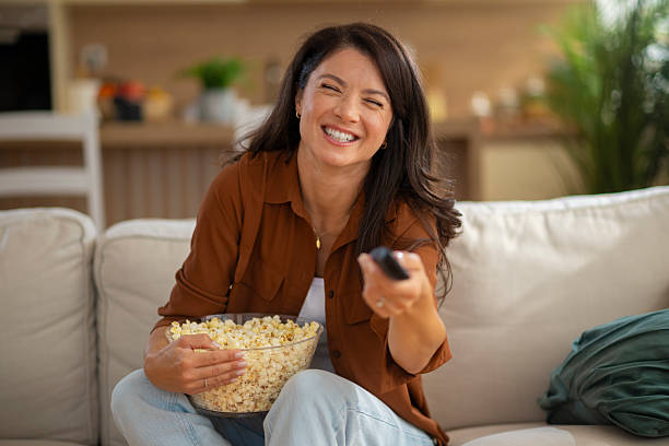 istock Woman laughing watching tv holding popcorn and remote 2247895164