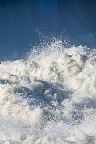 Strong powerful stream of rushing river water flows fast creating white foam and splashes against the deep blue background for a beautiful abstract natural texture of liquid energy outdoors