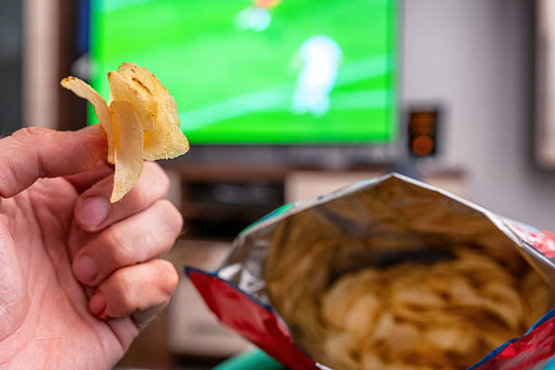 istock Eating chips from big package in front of television 2247900327