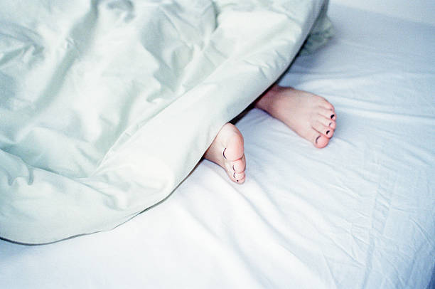Child feet under the white blanket under soft morning light