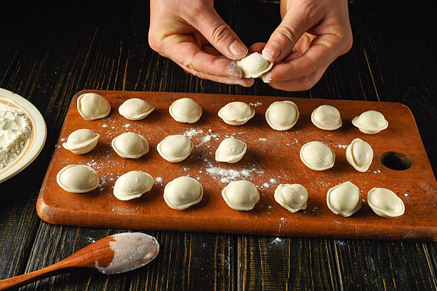 istock Hands skillfully shape dumplings on a wooden board dusted with flour. The kitchen atmosphere is warm and inviting, perfect for cooking traditional dishes 2247907605