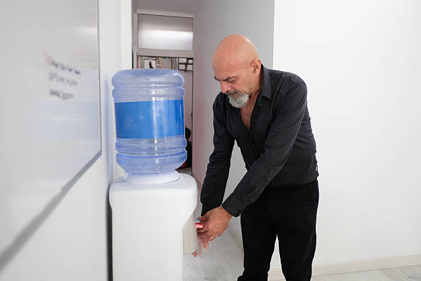 A 64-year-old man drinks water from the machine in his office.