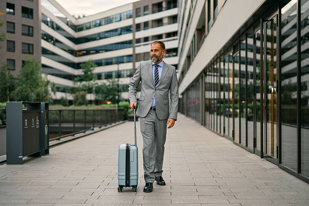 istock Businessman pulling luggage walking along modern office building 2247909062