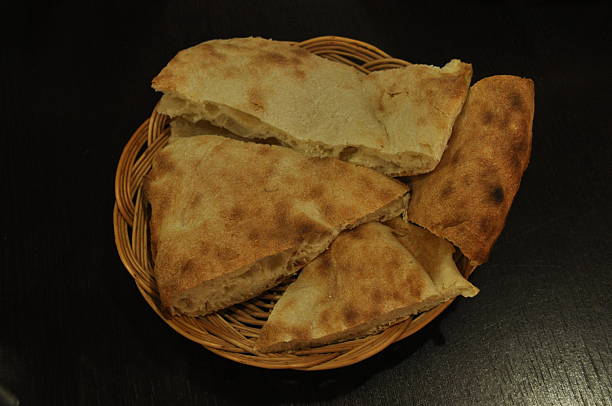 A basket holds warm, freshly baked bread pieces with a golden crust, placed on a dark table in a cozy restaurant setting during dinner. The inviting aroma fills the air.