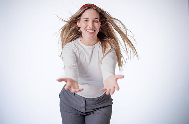 A cheerful woman is smiling and extending her arms forward, inviting engagement. Her long hair flows freely, complementing the bright and simple white background.
