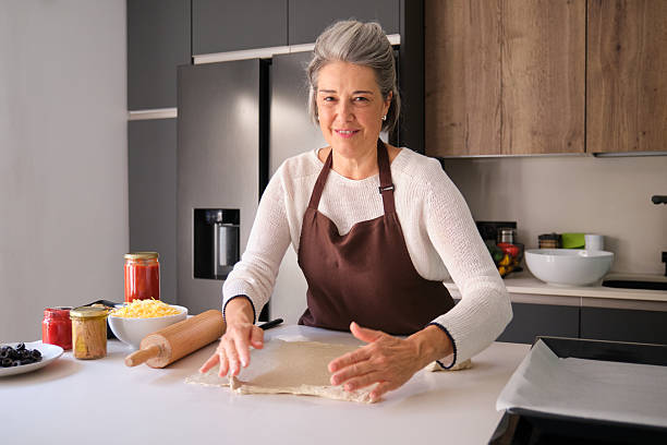 istock Senior woman smiling while preparing homemade pizza dough 2247915641