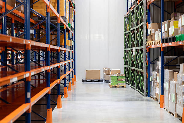 istock A wide aisle in a modern logistics warehouse features empty industrial racks. Opposite, other racks are filled with cardboard boxes. Several boxes on pallets wait on the concrete floor for stocking. 2247922767