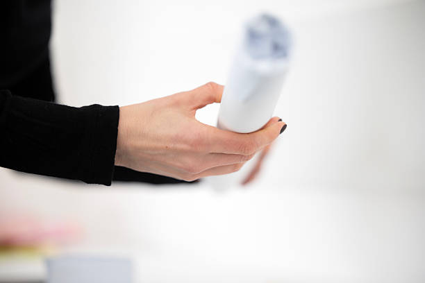 istock A woman's hand, with black nail polish, holds a rolled-up white paper document. This could be an architectural blueprint, a technical drawing, or a plan being reviewed in a bright office. 2247922881