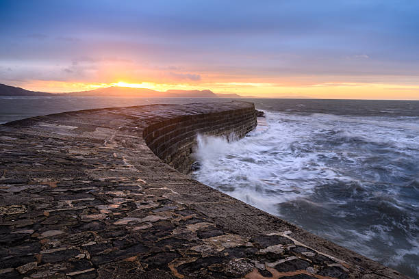 Sunrise at The Cobb on Lyme Regis with dramatic crashing waves in the ocean. Dorset, England, UK.