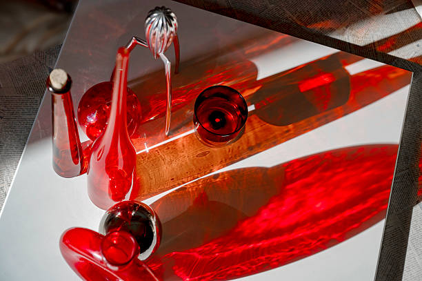 Still life with red glass bottles, top view, long bright shadows on a white table.