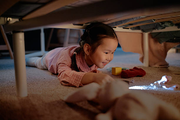 istock Asian Girl Child Lying under Bed Playing with Flashlight in Cozy Home Evening 2247937134