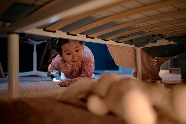 istock Asian Child Girl Smiling While Crawling under Bed Reaching for Stuffed Toy 2247937256