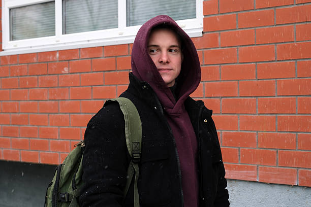 istock Young man in hoodie backpack standing by brick wall 2247946085