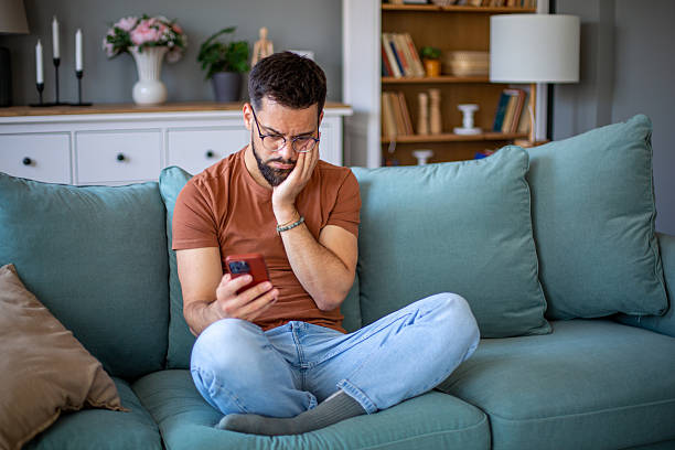 istock Young adult man feeling stressed looking at phone on couch 2247953206