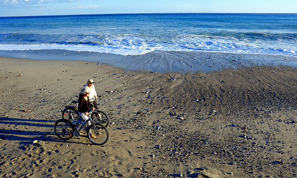 istock Mature women walk bicycles on beach at sunset 2247955329