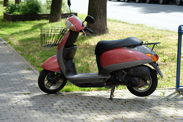Old red metal toy scooter, seen from the front, missing its handles and tires. This classic kids' plaything displays broken parts and signs of age.