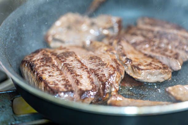 Detailed close-up of a person's gloved hand carefully placing a freshly cooked, juicy beef steak onto shiny aluminum foil for resting