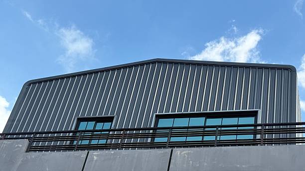 Clean exterior view of a contemporary office building constructed with corrugated metal sheet panels, rounded corner detail and blue‑tinted glazing against a clear sky. Concepts: industrial architecture, metal cladding, steel structure, prefab building, warehouse office conversion, minimal design.