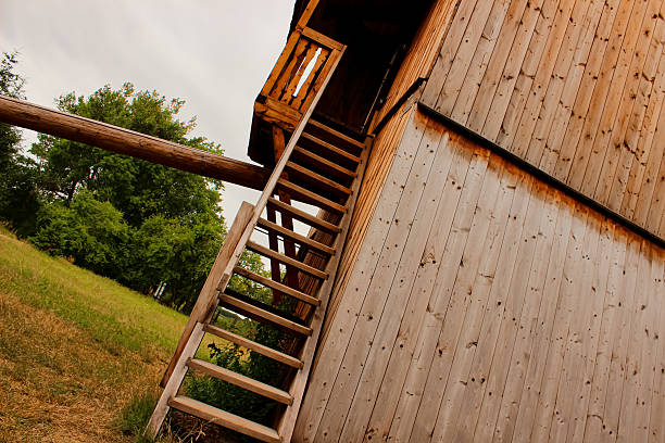 A traditional Slavic-style wooden windmill with a vertical plank facade, standing on a grassy slope in a rural setting.