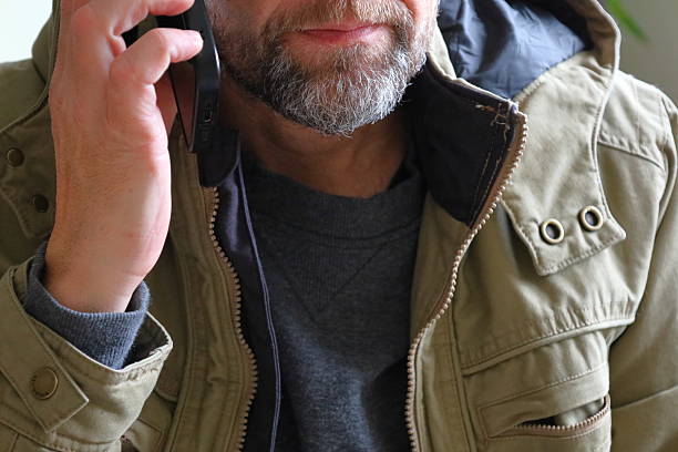 Close-up of a bearded man in a casual jacket holding a smartphone to his ear while speaking, showing communication and everyday lifestyle moments.
