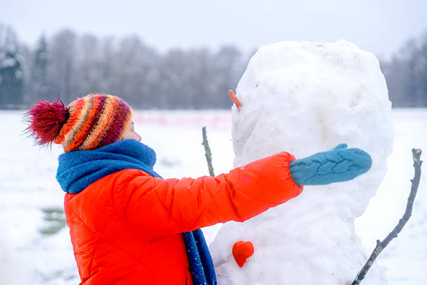 A child in a bright winter jacket builds a snowman with care in a snowy field, enjoying the cold weather and the fun of snow play during the winter season.