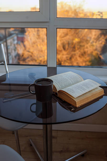 istock Coffee and a book on a table by a window with a view of autumn trees 2247977900