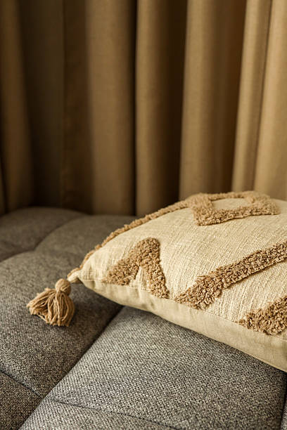 Decorative pillow with tassel on a gray sofa against a neutral curtain backdrop