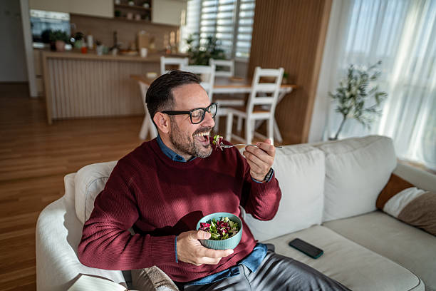 istock Man enjoying healthy salad lunch relaxing on couch 2247982609