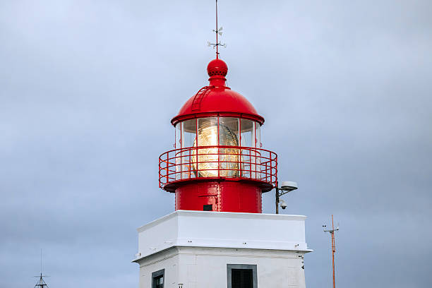 Red lighthouse with a glass lantern, standing tall against a cloudy sky