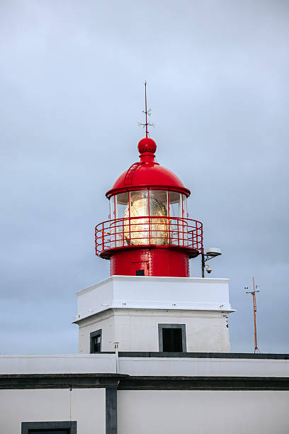 istock Red lighthouse with a glass lantern, standing tall against a cloudy sky 2247989101